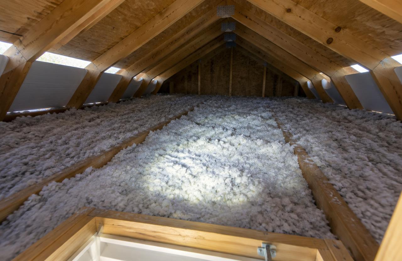 An attic seen from the hatch, with fluffy blown-in insulation between the joists and white baffles at the eaves letting light in