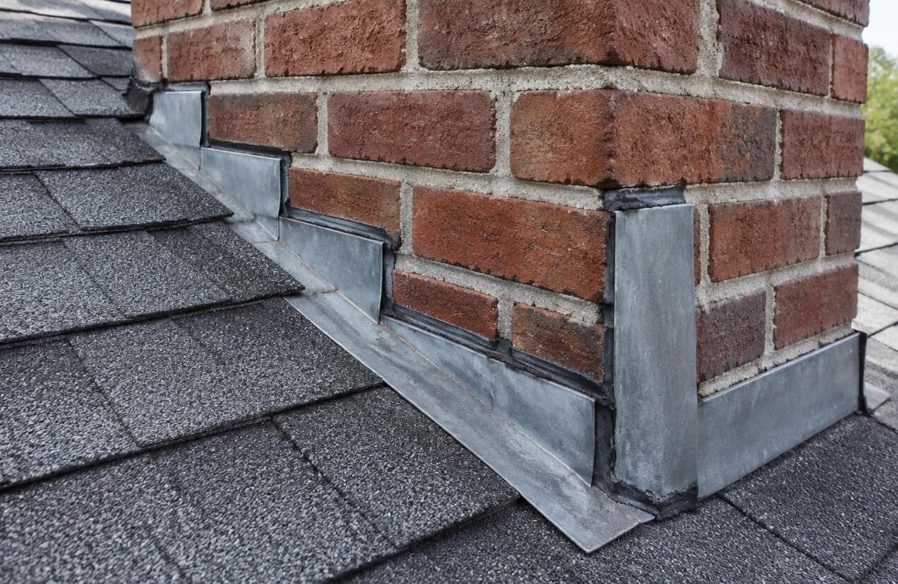 A brick chimney on a shingle roof with metal step flashing and counterflashing tucked into the mortar joints