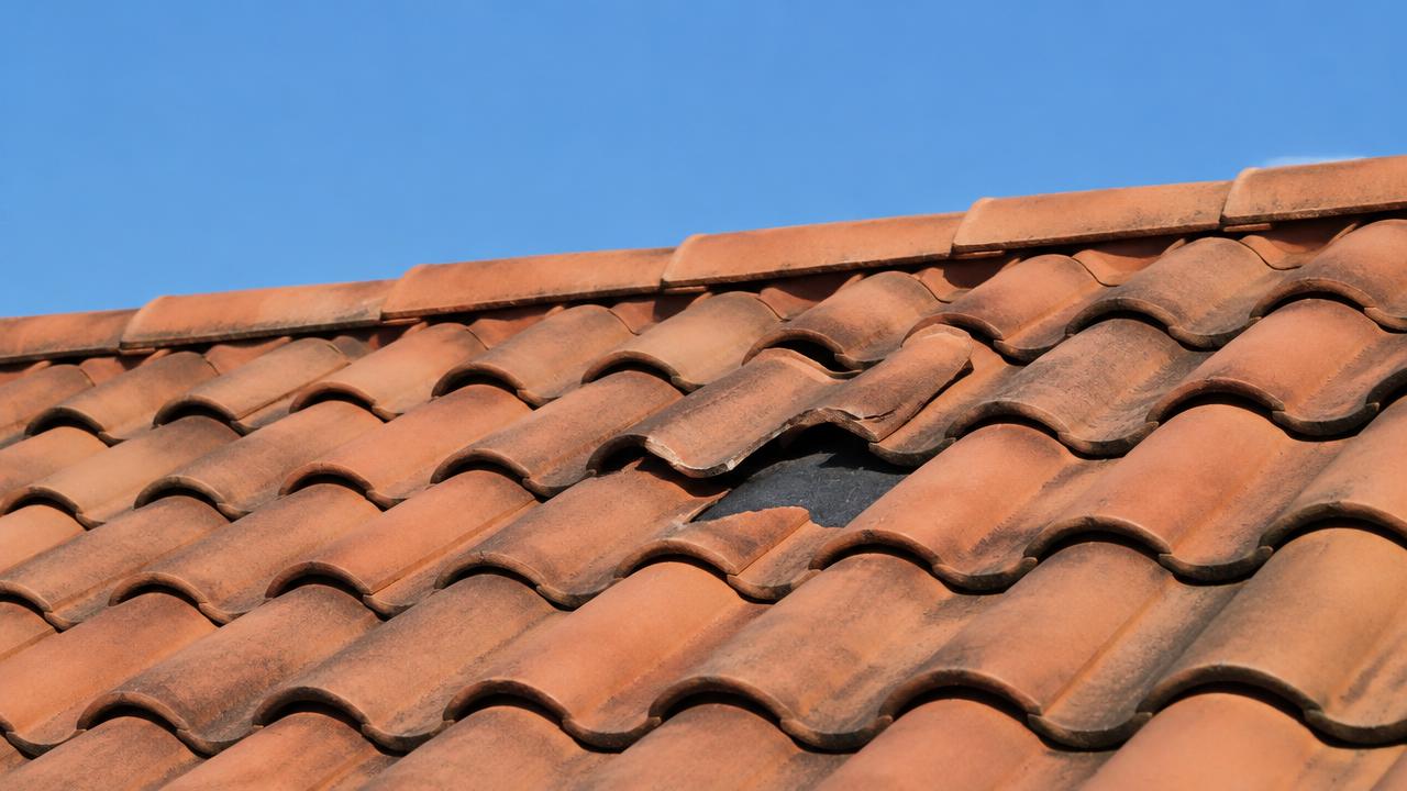 Orange clay S-shaped roof tiles on a house, with one broken tile showing the dark underlayment beneath it