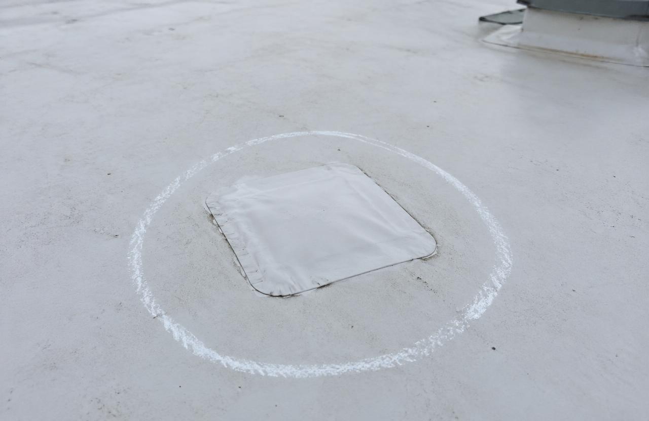 A small square patch welded onto a white single-ply flat roof, circled in chalk to mark the repair