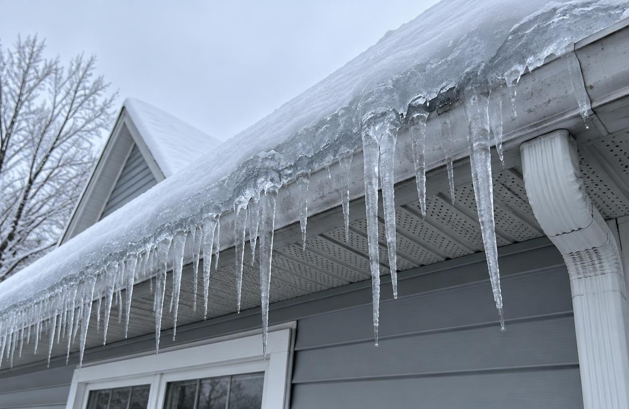 A thick ridge of ice along a snowy roof edge with long icicles hanging from the gutter
