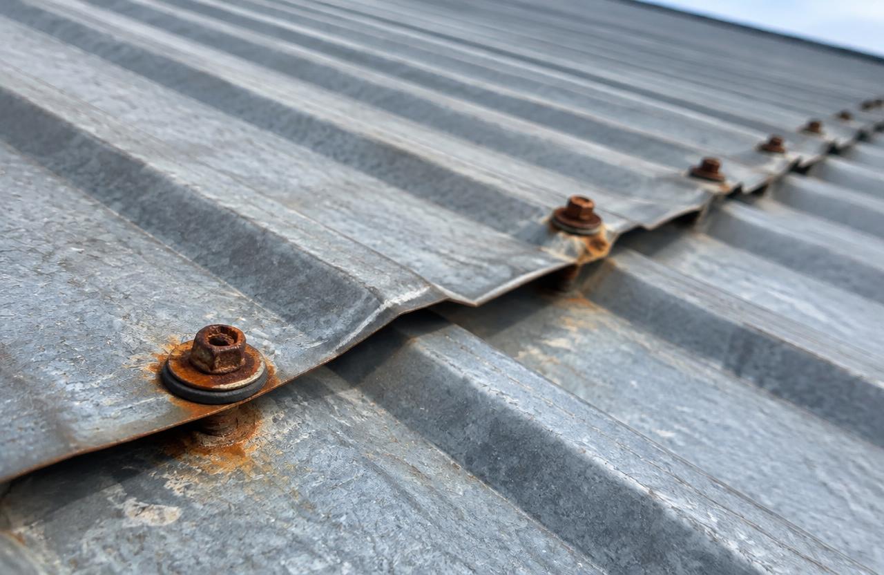 Close view of rusty screw heads and worn rubber washers along a lap on an exposed-fastener metal roof