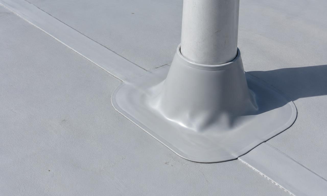 Close view of a light gray PVC roof membrane with a heat-welded seam and a molded boot sealed around a pipe